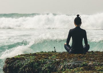 Yoga woman meditation at the seaside cliff edge facing the coming strong sea waves